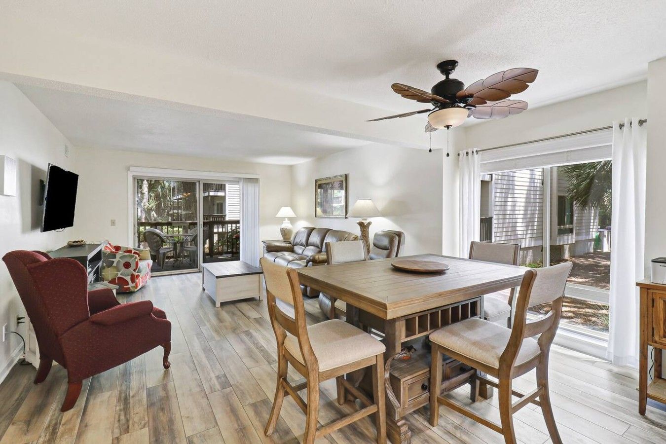 A spacious living area with a wooden dining table, leather chairs, a red armchair, and a ceiling fan.
