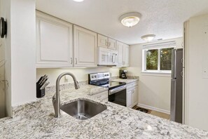 A kitchen with white cabinets, a stainless steel sink, a microwave, an oven, and a refrigerator.