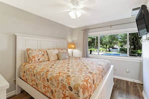 Ein Schlafzimmer mit einem Bett, einem Deckenventilator, einem Fenster mit Ausblick ins Freie und einem an der Wand befestigten Fernseher.