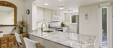 A kitchen with a granite countertop, white cabinets, a sink, a stove, and a refrigerator.