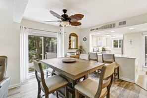 A dining area with a wooden table and chairs, a ceiling fan, and a view of the outdoors.