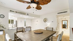Un comedor con una mesa de madera, sillas, un ventilador de techo y un reloj en la pared.