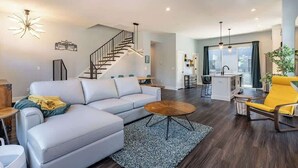 Un salon moderne avec un canapé bleu clair, une table basse en bois et un fauteuil jaune. Un escalier avec une rampe en métal mène à un niveau supérieur.