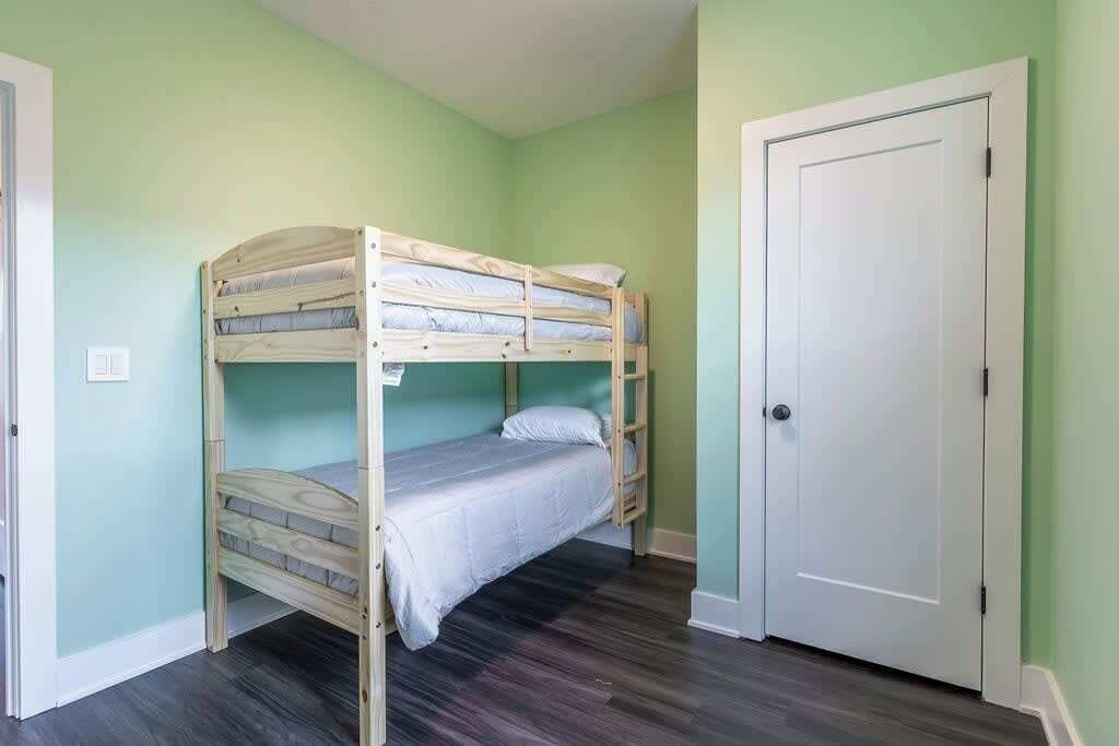 Une pièce avec un lit superposé, une porte blanche et des murs vert clair.