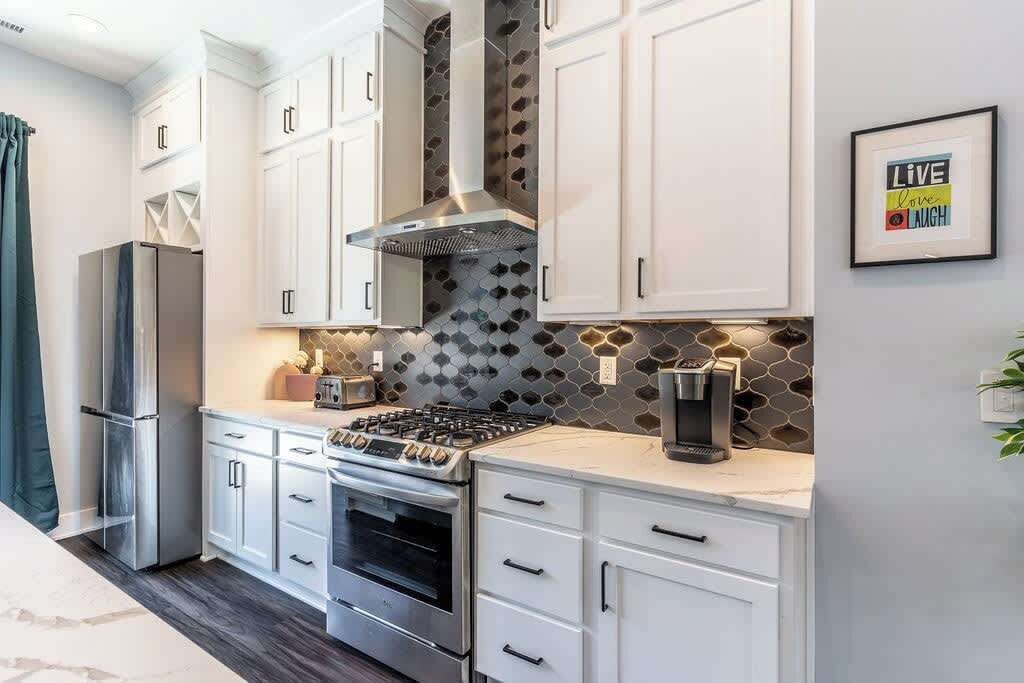 A modern kitchen with white cabinets, a stainless steel range, and a hexagonal backsplash.
