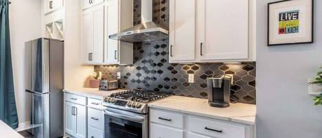 A modern kitchen with white cabinets, a stainless steel range, and a hexagonal backsplash.