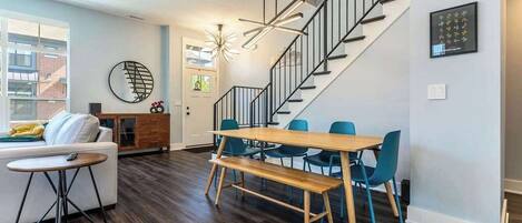 A modern living room with a dining area, a staircase, and a view of the outside.
