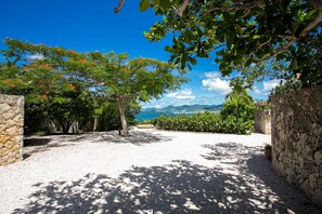 Un sendero de grava que conduce a un muro de piedra, con vista al mar y montañas al fondo.