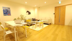 A modern, well-lit room with a wooden floor, a white table with a laptop, yellow chairs, a grey sofa, and a wooden door. - Acro Capsule Hotel Namba Dotonbori (Osaka)