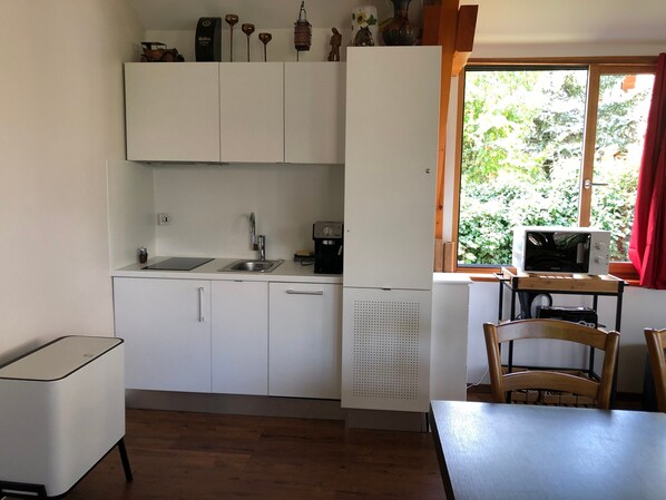 Una cucina compatta con mobili bianchi, un lavello, una macchina da caffè e un forno a microonde su un tavolo di legno.