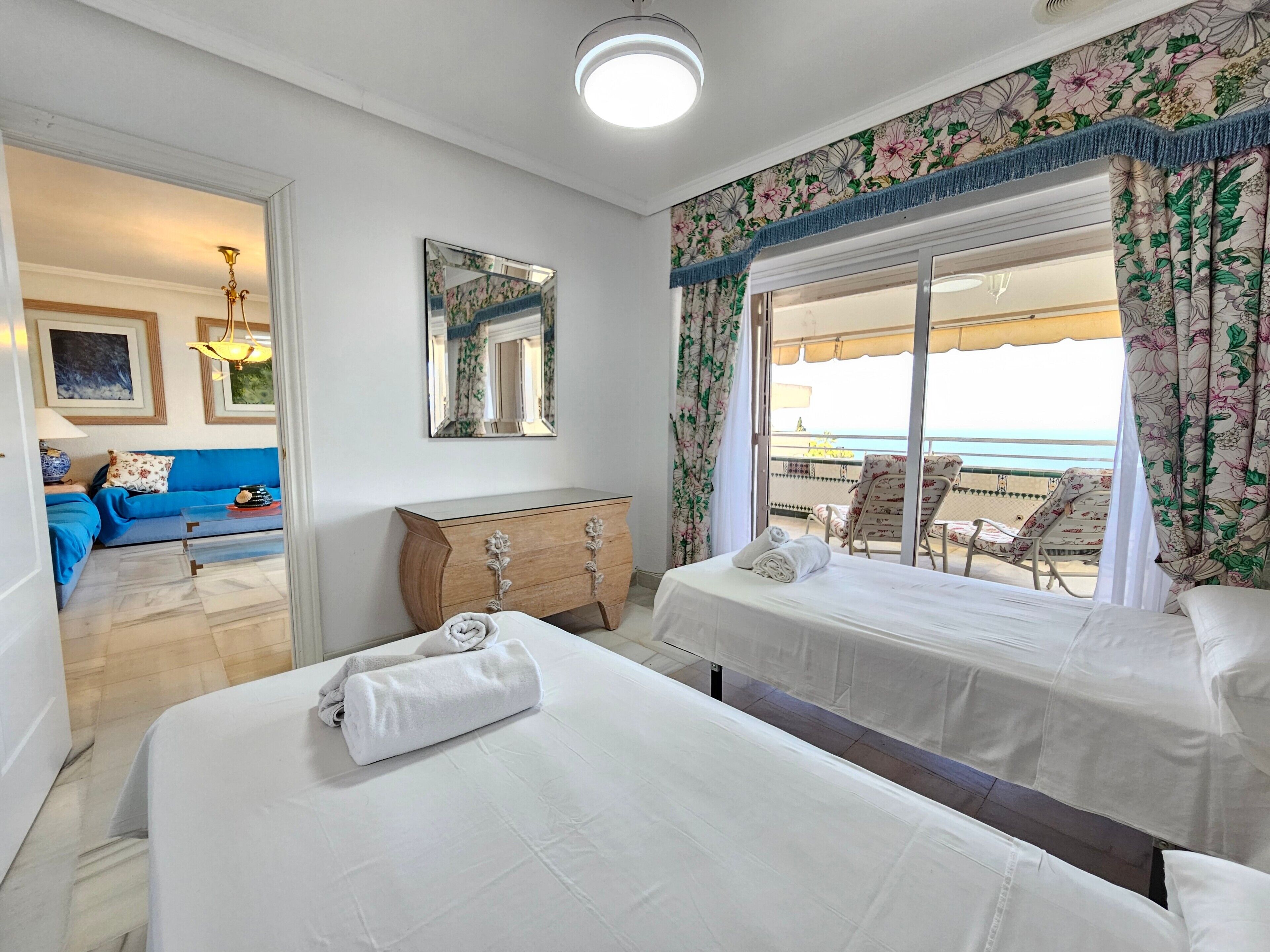 Een hotelkamer met twee bedden, een sofa, een dressoir en een balkon met uitzicht.