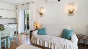 A living room with a sofa, a table, and a lamp. There is a kitchen area with cabinets and a window. - Holiday Apartment "Villa Isabella Casa Lucia" with Sea View, Shared Terrace & Wi-Fi (Imperia)