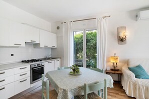 Une cuisine moderne avec des meubles blancs, une table à manger agrémentée d’une plante verte en guise de centre de table, et un coin salon confortable avec une lampe.