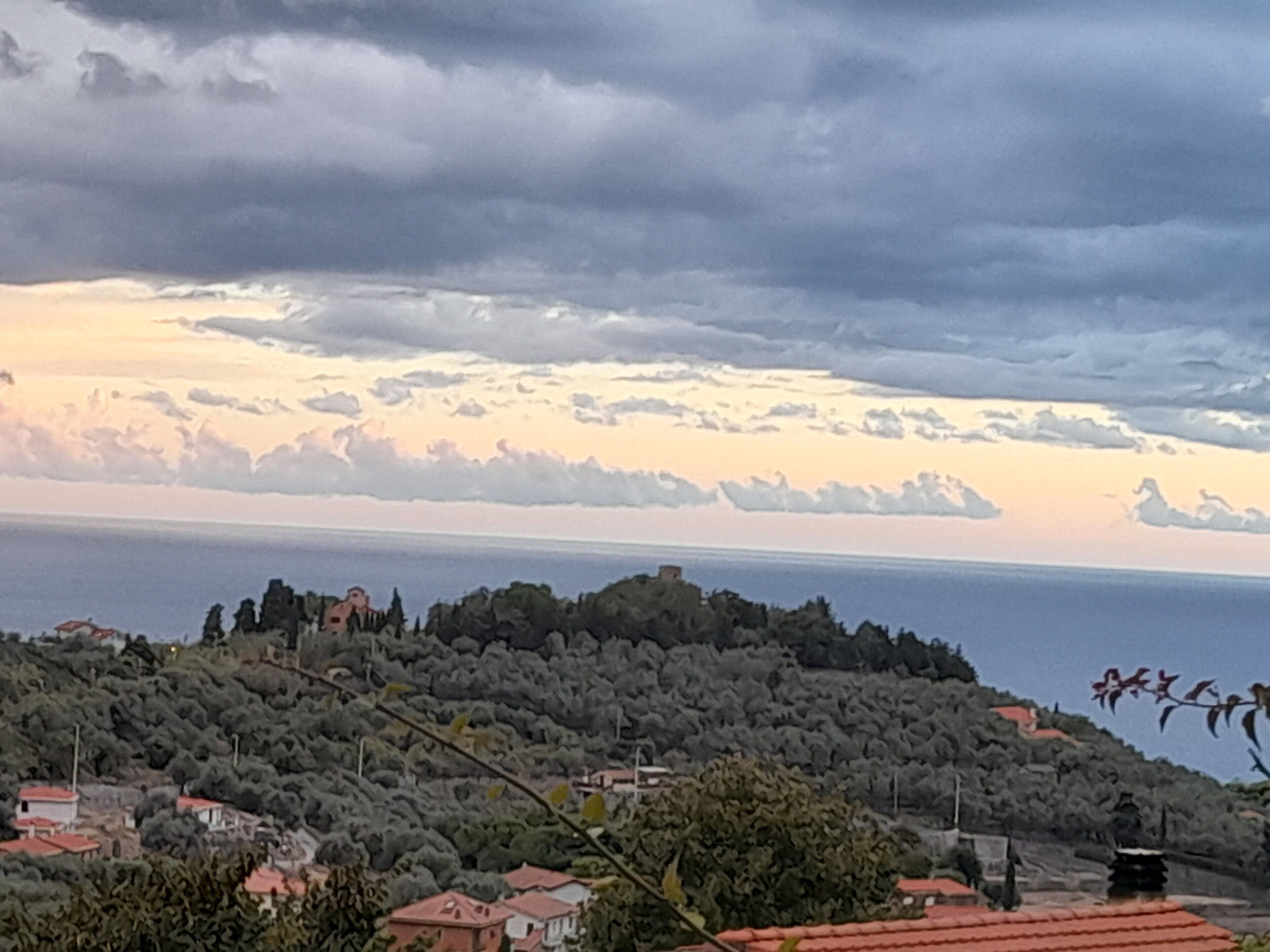 A coastal landscape with a village on a hill, houses with red roofs, and a view of the sea.