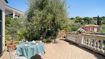 Eine Terrasse mit Tisch für zwei Personen, umgeben von Topfpflanzen und einem großen Baum.