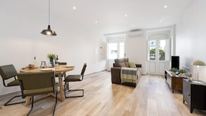 A modern living room with a dining area, wooden flooring, and a large window.