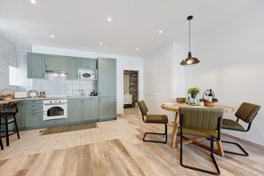 Una cucina moderna con pensili verde chiaro, forno bianco e zona pranzo con tavolo rotondo e due sedie.