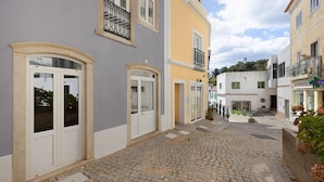 A cobblestone street with buildings, a visible door, and a window with a balcony.