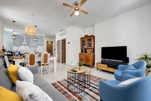 Een moderne woonkamer met een bank, fauteuils, een salontafel, een televisie en een plafondventilator.
