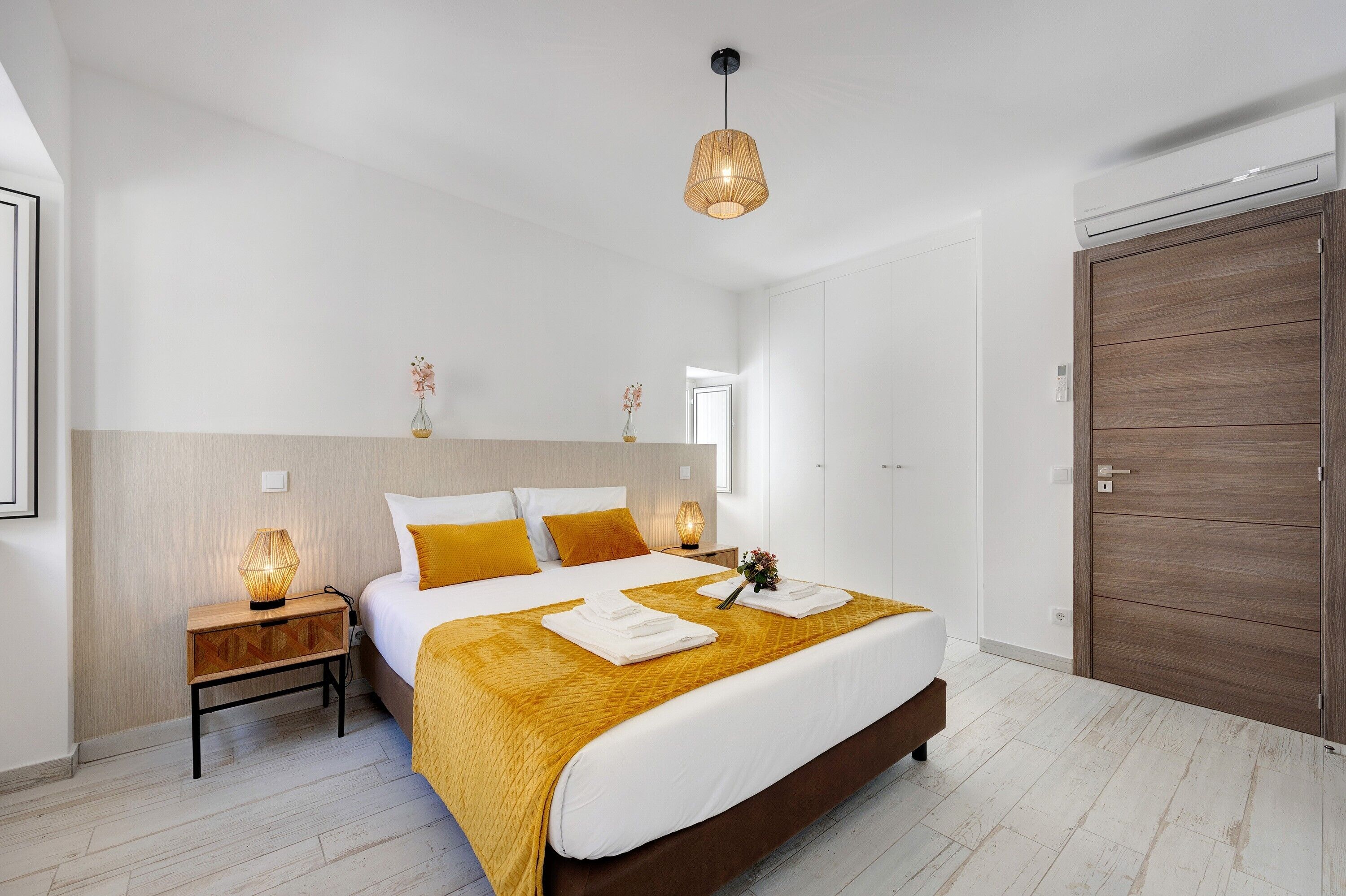 A modern bedroom with a large bed, bedside lamps, a wooden wardrobe, and a hanging light fixture.
