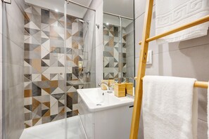 Een moderne badkamer met een betegelde spatwand in geometrische patronen, een wit wastafelmeubel en een houten handdoekhouder.