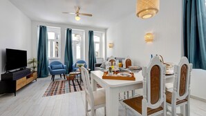 Un salon moderne doté d’un téléviseur à écran plat, d’un coin repas avec une table et des chaises blanches, et d’un ventilateur de plafond.