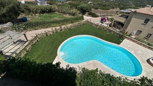 A swimming pool surrounded by a well-maintained lawn, with a view of the sea and hills in the background.