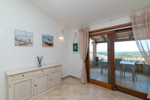 A room with a sliding glass door leading to an outdoor terrace, a cabinet with drawers, and two framed paintings on the wall.