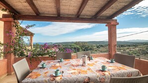 An outdoor patio with a table set for two, surrounded by wicker chairs, with a view of the countryside. - Holiday Apartment "La Rosa dei Venti" with Sea View, Shared Pool & Private Terrace (Santa Teresa Gallura)