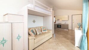 A room with a bunk bed, a sofa with decorative pillows, a kitchenette, and a bathroom with a shower curtain. - Holiday Apartment "La Rosa dei Venti" with Sea View, Shared Pool & Private Terrace (Santa Teresa Gallura)