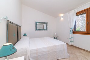 Un dormitorio con cama, mesita de noche, lámpara, espejo y ventana con cortinas.