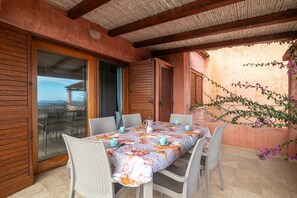 Une terrasse extérieure avec une table dressée pour quatre personnes, entourée de chaises en osier, et une vue à travers une porte vitrée.