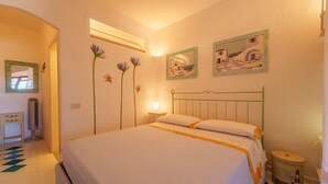 A neatly arranged bedroom with a bed, bedside table, lamp, and wall decorations including framed pictures and floral designs.