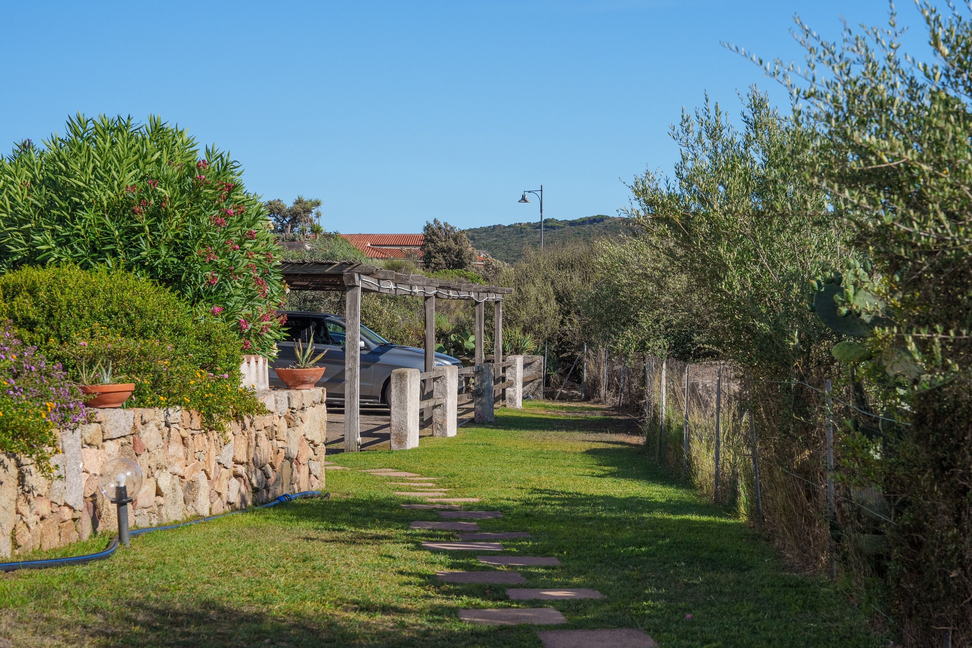 A stone wall, a wooden pergola, and a pathway leading to a vehicle.