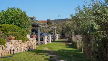 A stone wall, a wooden pergola, and a pathway leading to a vehicle.