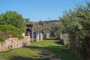 Un muro de piedra, una pérgola de madera y un sendero que lleva a un vehículo.