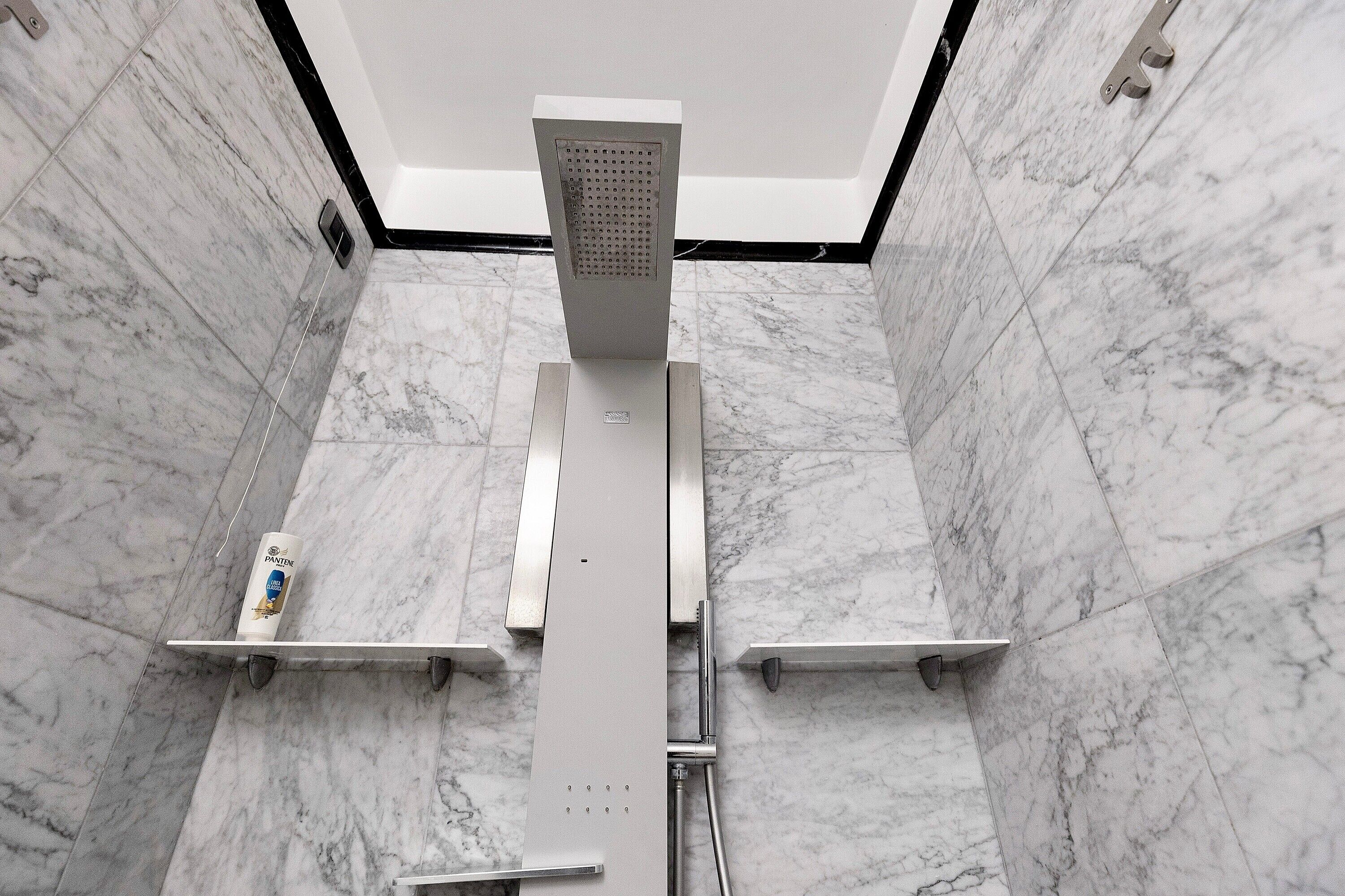 Un baño moderno con ducha, paredes de mármol e iluminación en el techo.