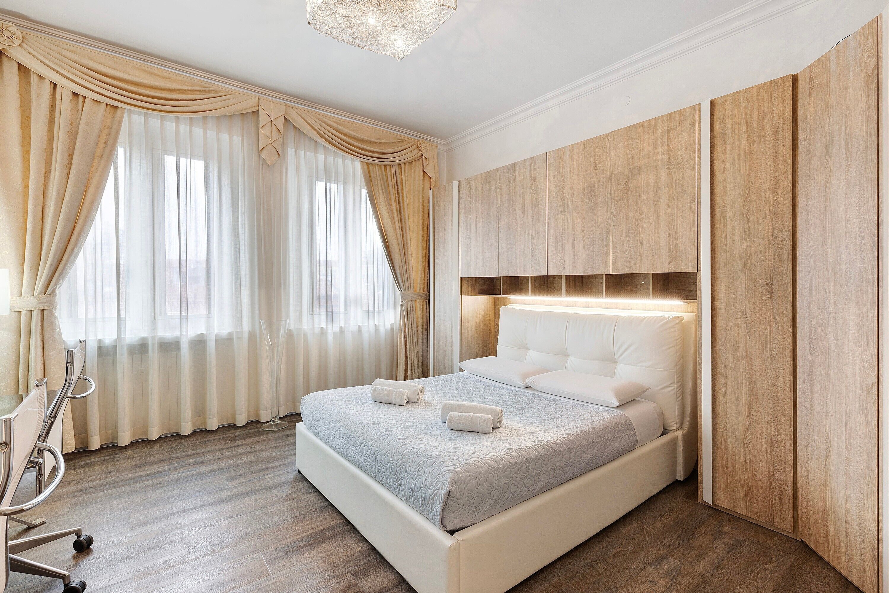 Een netjes ingerichte slaapkamer met een bed, gordijnen, een nachtkastje en een houten garderobe.