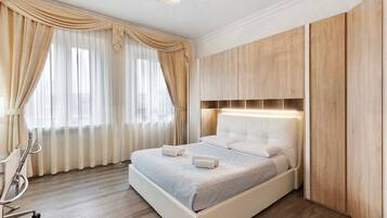 Een netjes ingerichte slaapkamer met een bed, gordijnen, een nachtkastje en een houten garderobe.