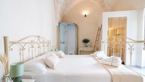 Ein Schlafzimmer mit Bett, Nachttisch, Lampe, Spiegel, Kleiderschrank und Dusche.