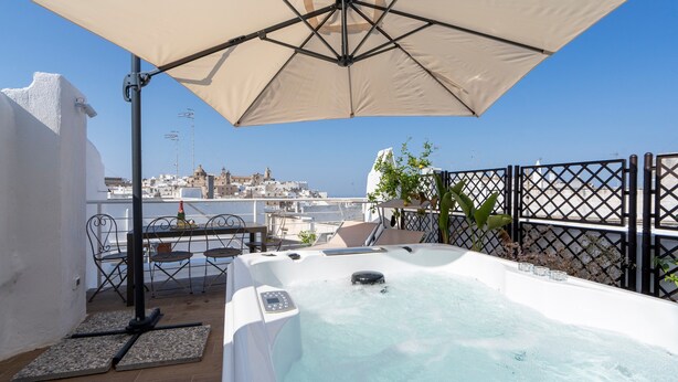 Eine Dachterrasse mit Whirlpool, Sitzgelegenheiten im Freien und Blick auf die Stadt.