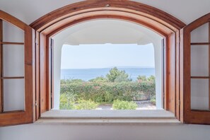 Een open raam met houten kozijn, met uitzicht op zee en groen.