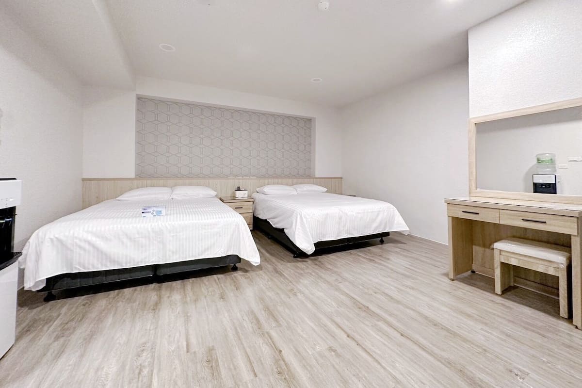 Quarto de hotel moderno com duas camas, uma escrivaninha de madeira, um espelho e um pequeno banco.
