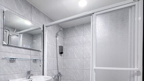Un baño moderno con cabina de ducha de vidrio, lavamanos pedestal y un espejo grande.