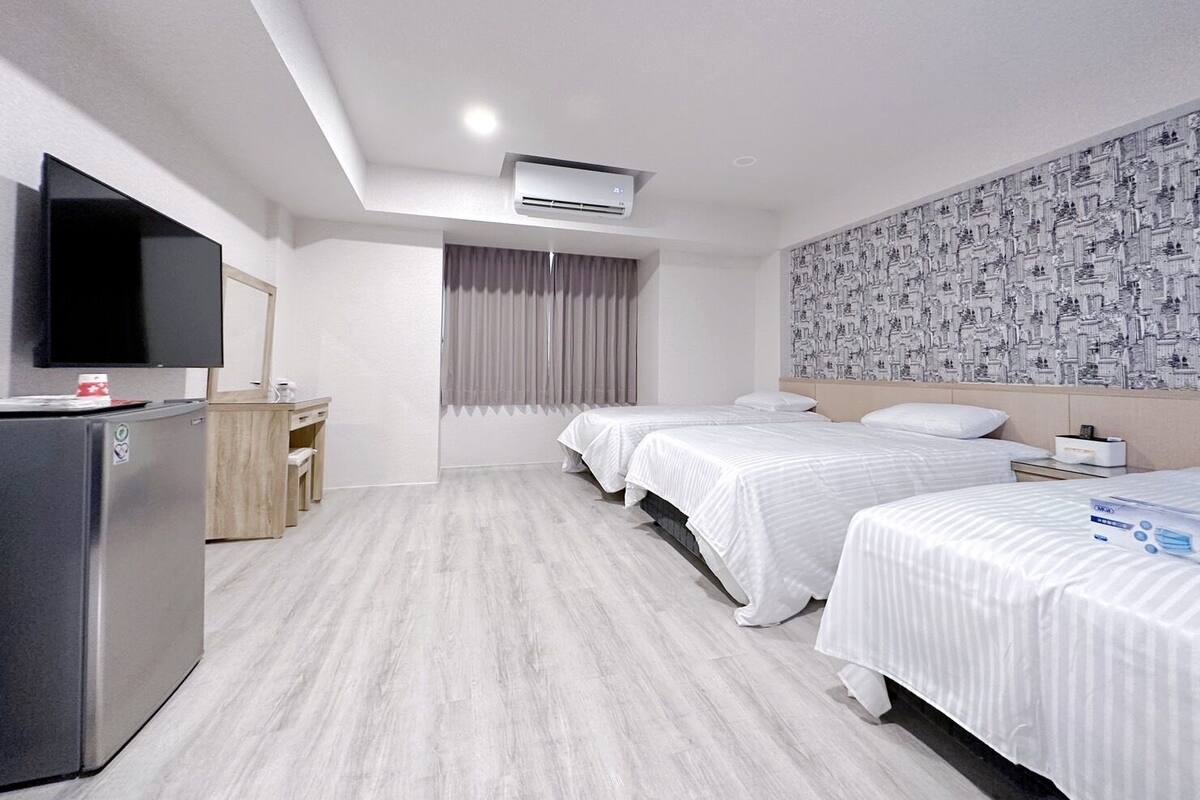 Quarto de hotel com duas camas, uma escrivaninha, televisão e papel de parede estampado.