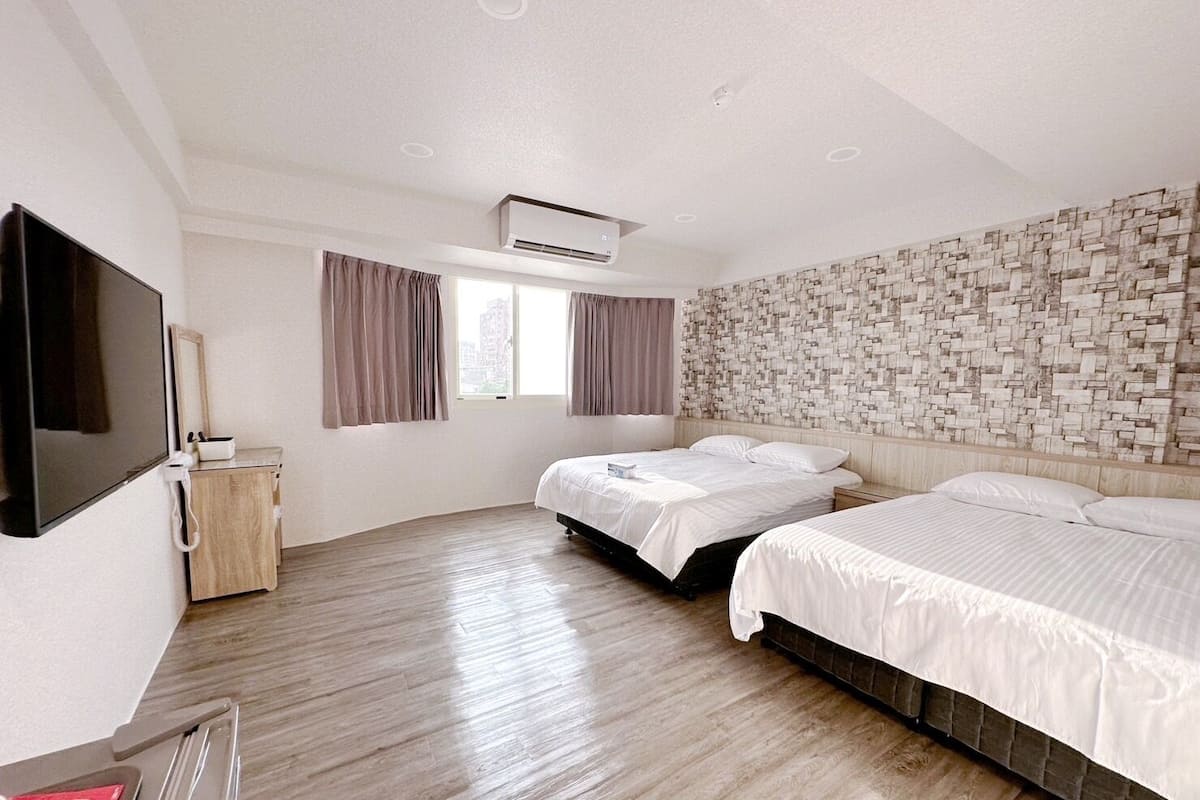 Quarto de hotel moderno com duas camas, televisão de tela plana, ar-condicionado, armário de madeira e janela com cortinas.
