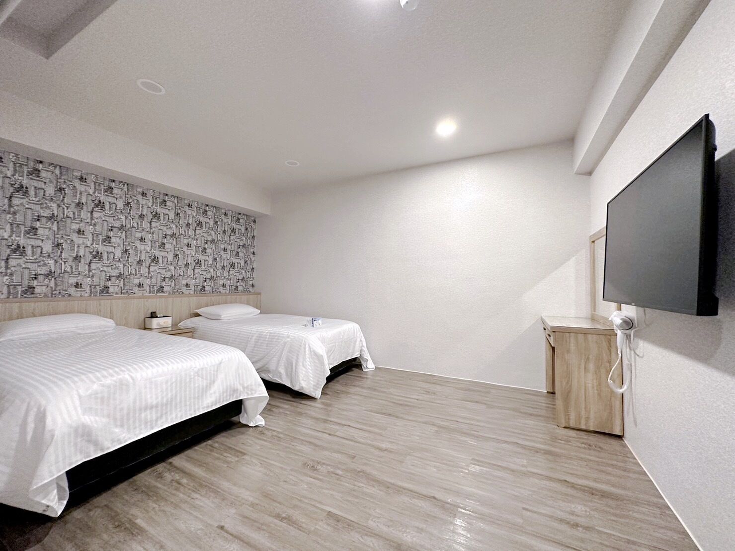 Une chambre d’hôtel moderne avec deux lits, un téléviseur à écran plat et un papier peint à motifs.