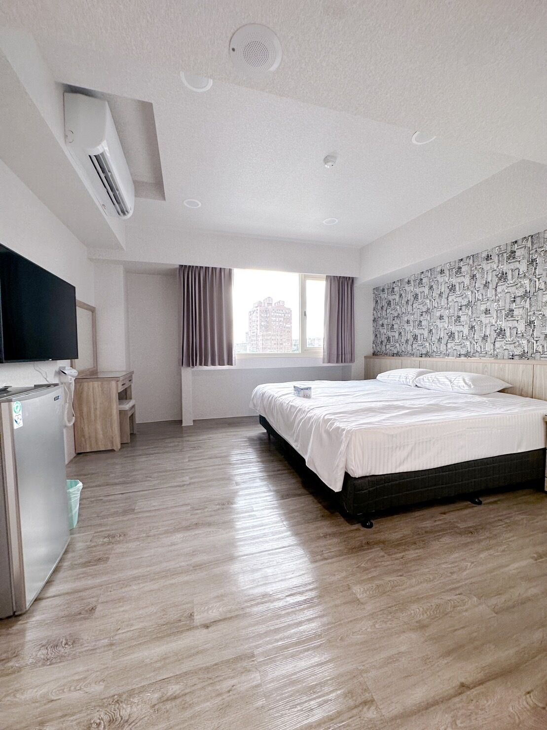 Ein Hotelzimmer mit Bett, Fernseher, Schreibtisch, Fenster und einer Wand mit Muster.