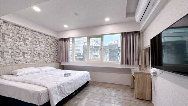 Un dormitorio moderno con una cama grande, televisor y ventana con cortinas.