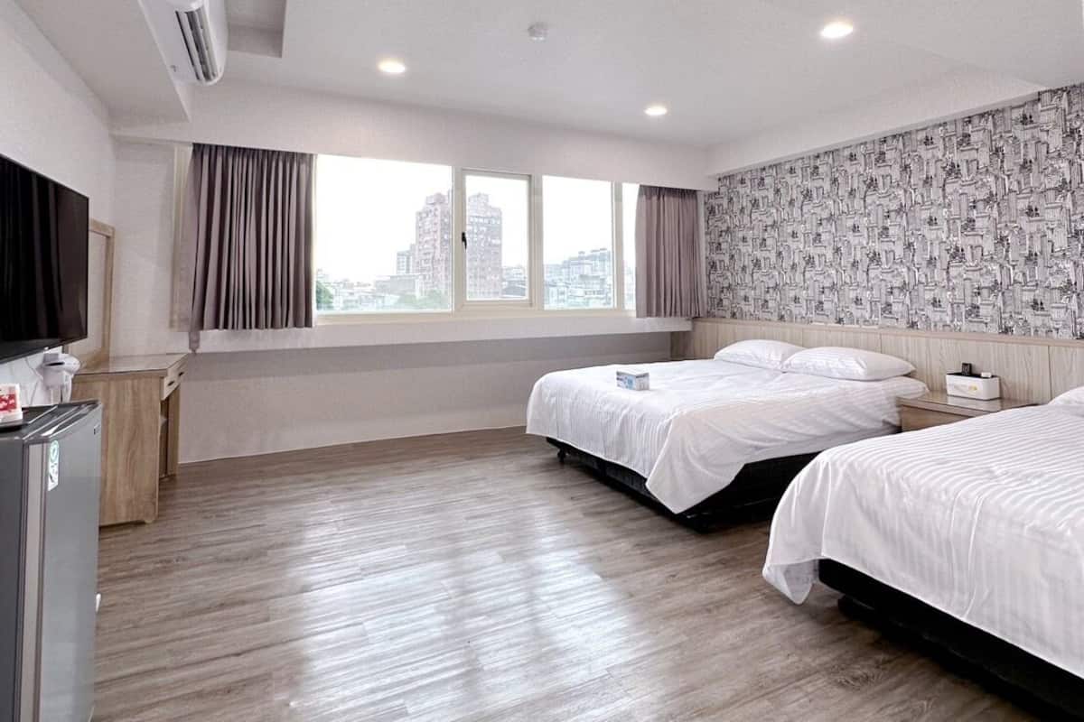Quarto de hotel com duas camas, uma escrivaninha pequena, um frigorífico e uma janela com cortinas.